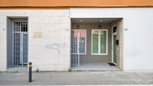 Una entrada de edificio con una reja metálica, una puerta con un cerrojo verde y un muro con un letrero con número.