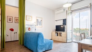 Moderni olohuone, jossa on sininen sohva, puulattia, ruokailutila ja näkymä lasiovesta.