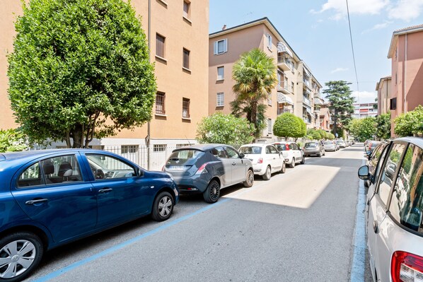 A street lined with parked cars and multi-story buildings with balconies.