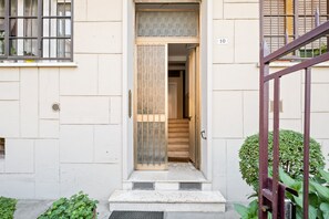 A building entrance with a wooden door, a metal gate, and a small garden area with plants.