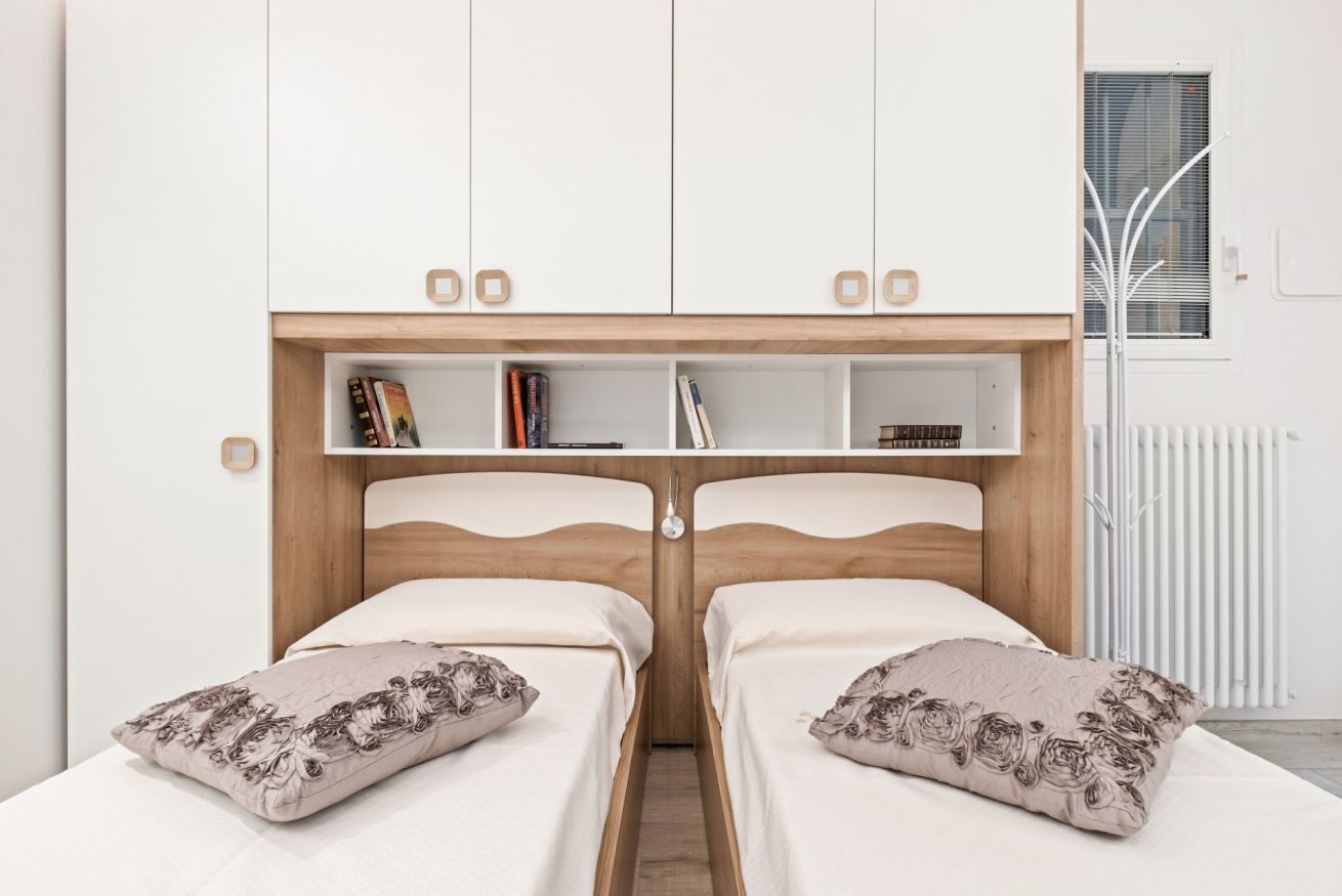 Une chambre avec deux lits, une tête de lit en bois, une étagère intégrée remplie de livres et un radiateur.