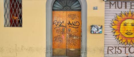 Una entrada de edificio con puerta de madera, ventana con barrotes y un mural en la pared.