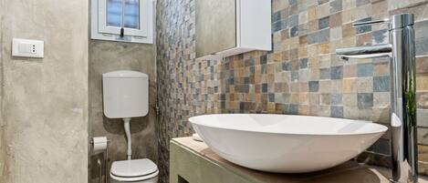 Un baño con inodoro blanco, un lavamanos blanco con una pileta grande y un salpicadero de azulejos.
