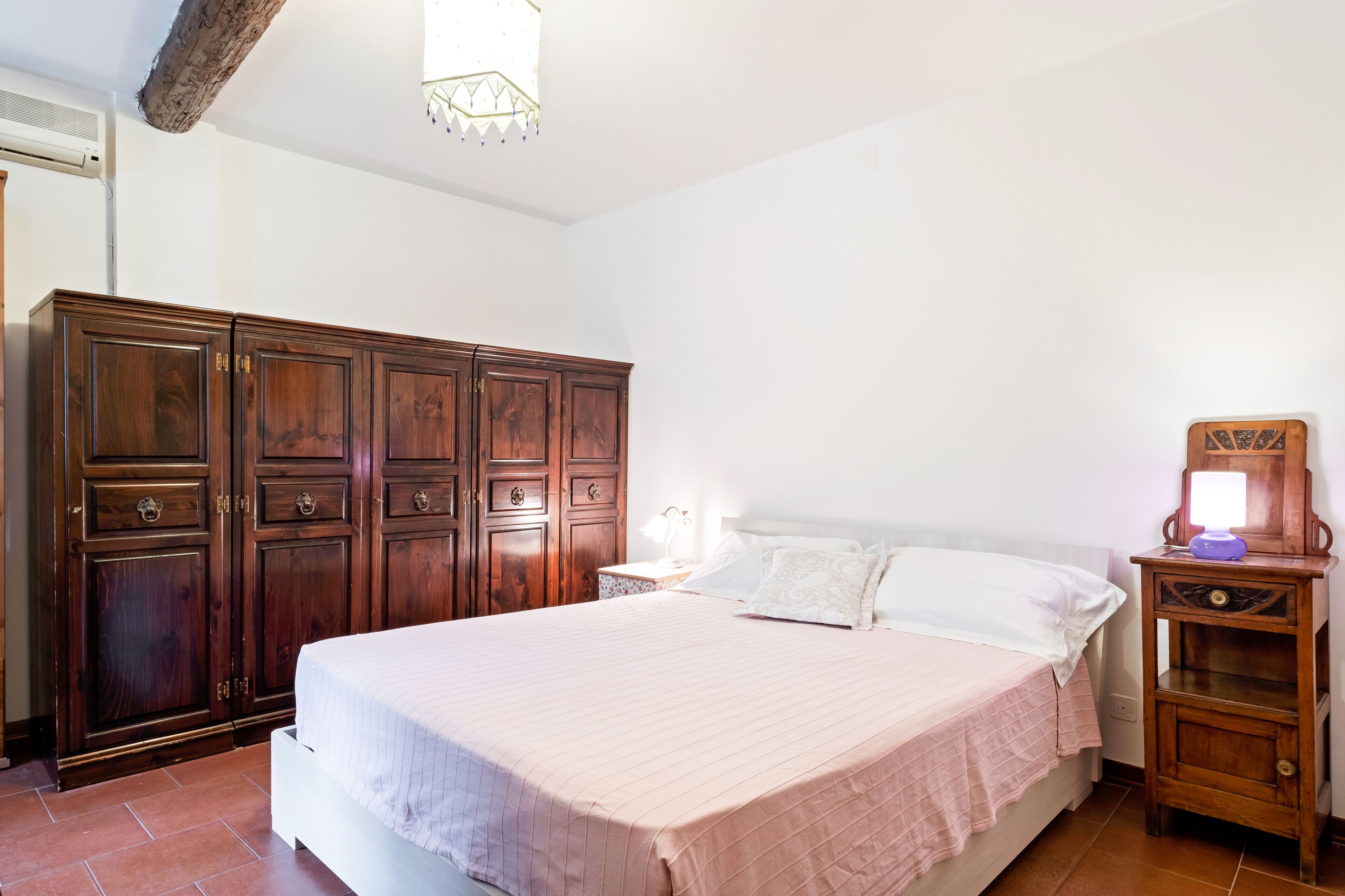 Un dormitorio con una cama grande, un armario de madera y una mesita de noche con lámpara.