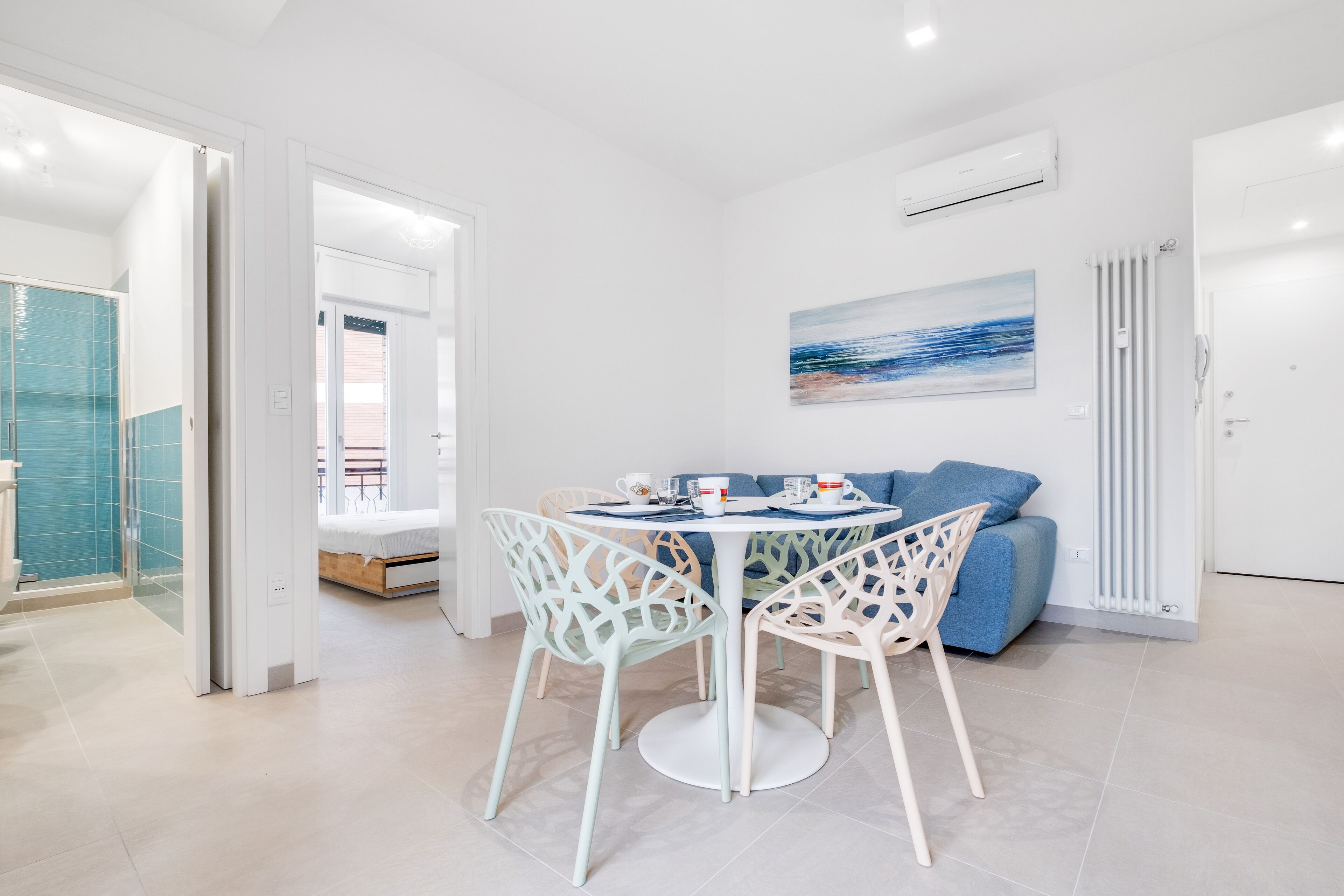 A modern room with a round dining table, white chairs, a sofa, and a painting on the wall.