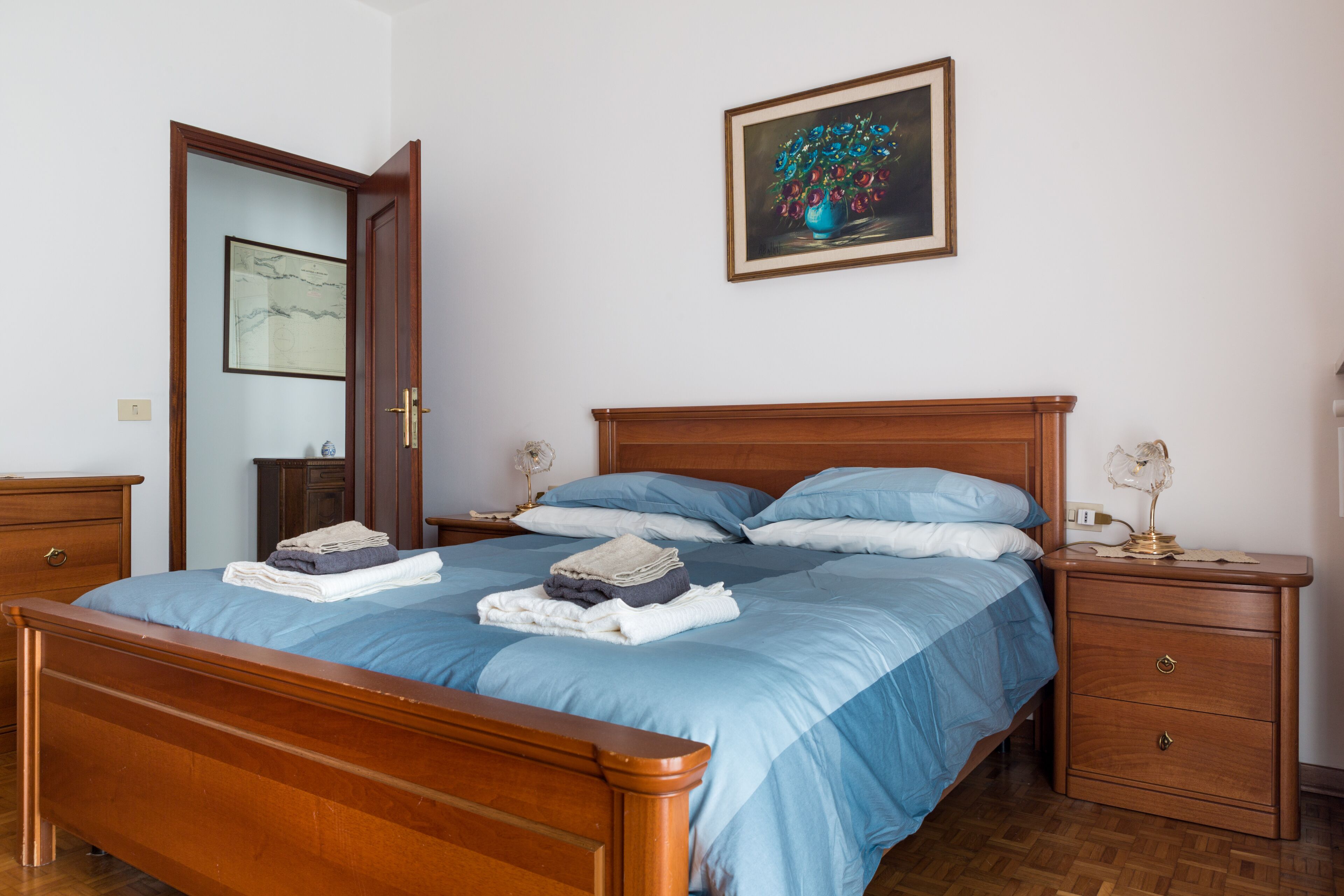 A neatly made bed with blue bedding, a wooden headboard, and a nightstand with a lamp.