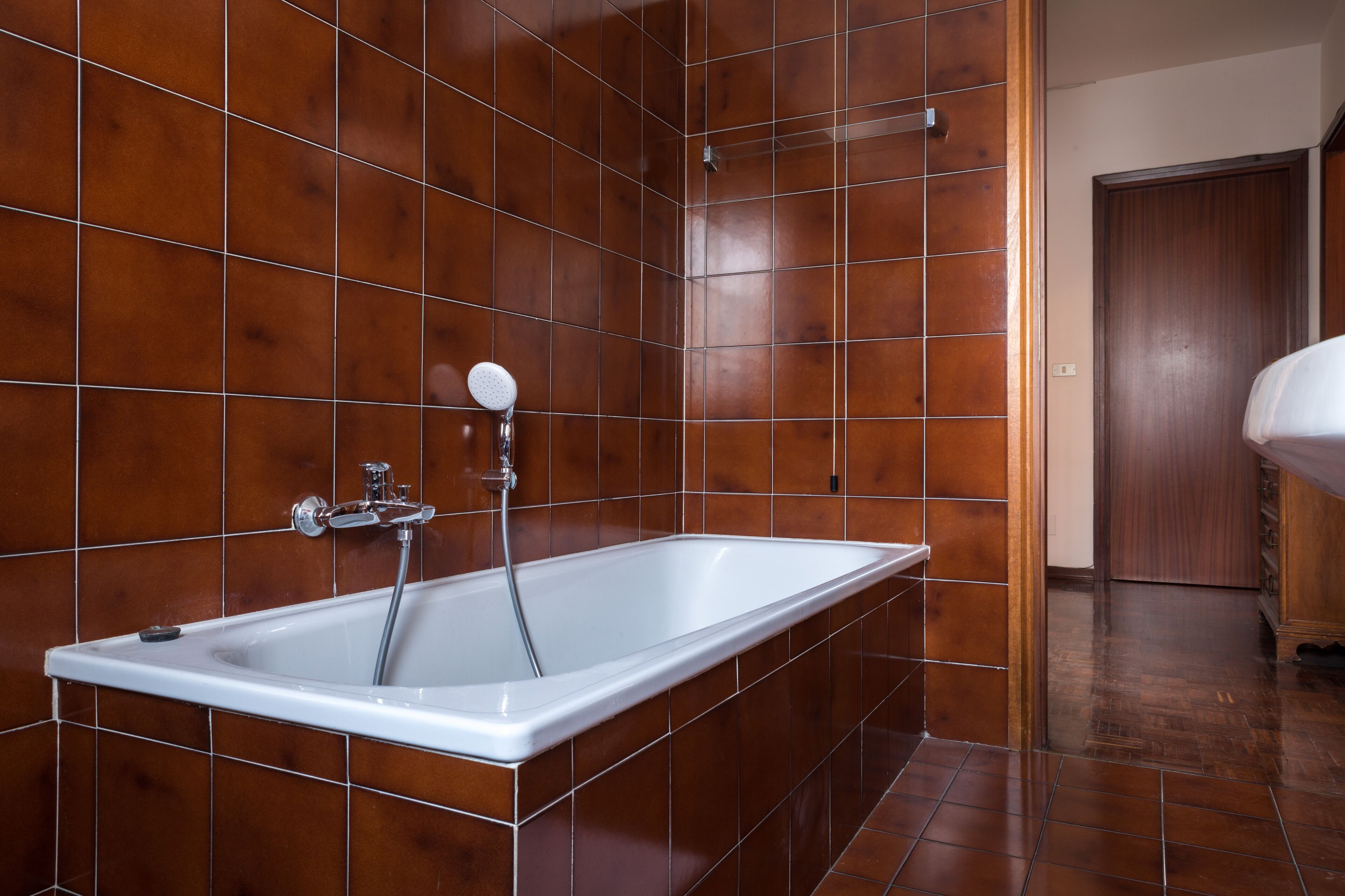 A modern bathroom with a rectangular bathtub, tiled walls, and a wooden door.