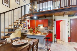 A modern kitchen with red cabinets, a wooden staircase, and a dining area with a table set for two.