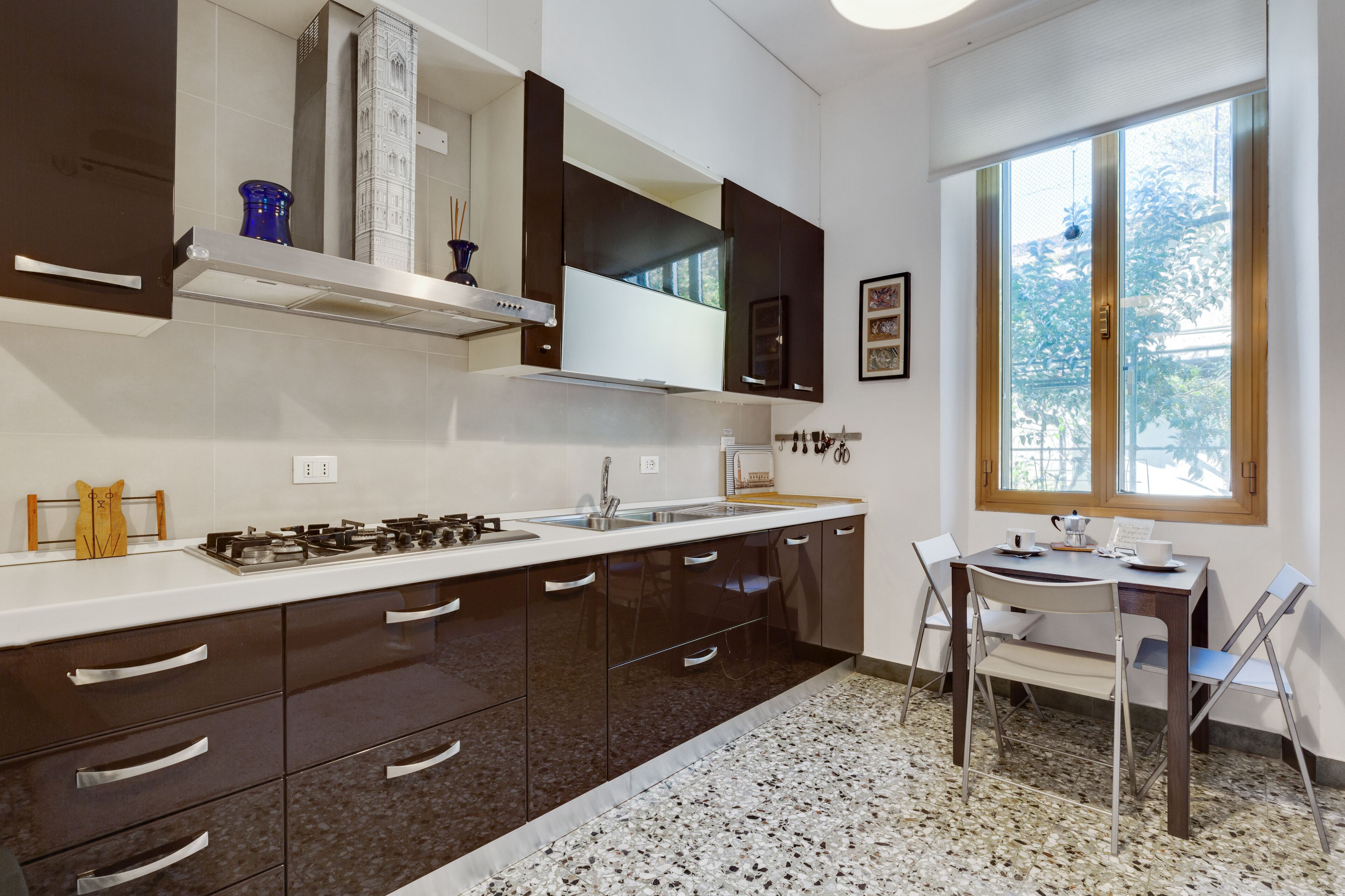 A modern kitchen with dark cabinetry, a white countertop, and a window providing natural light.