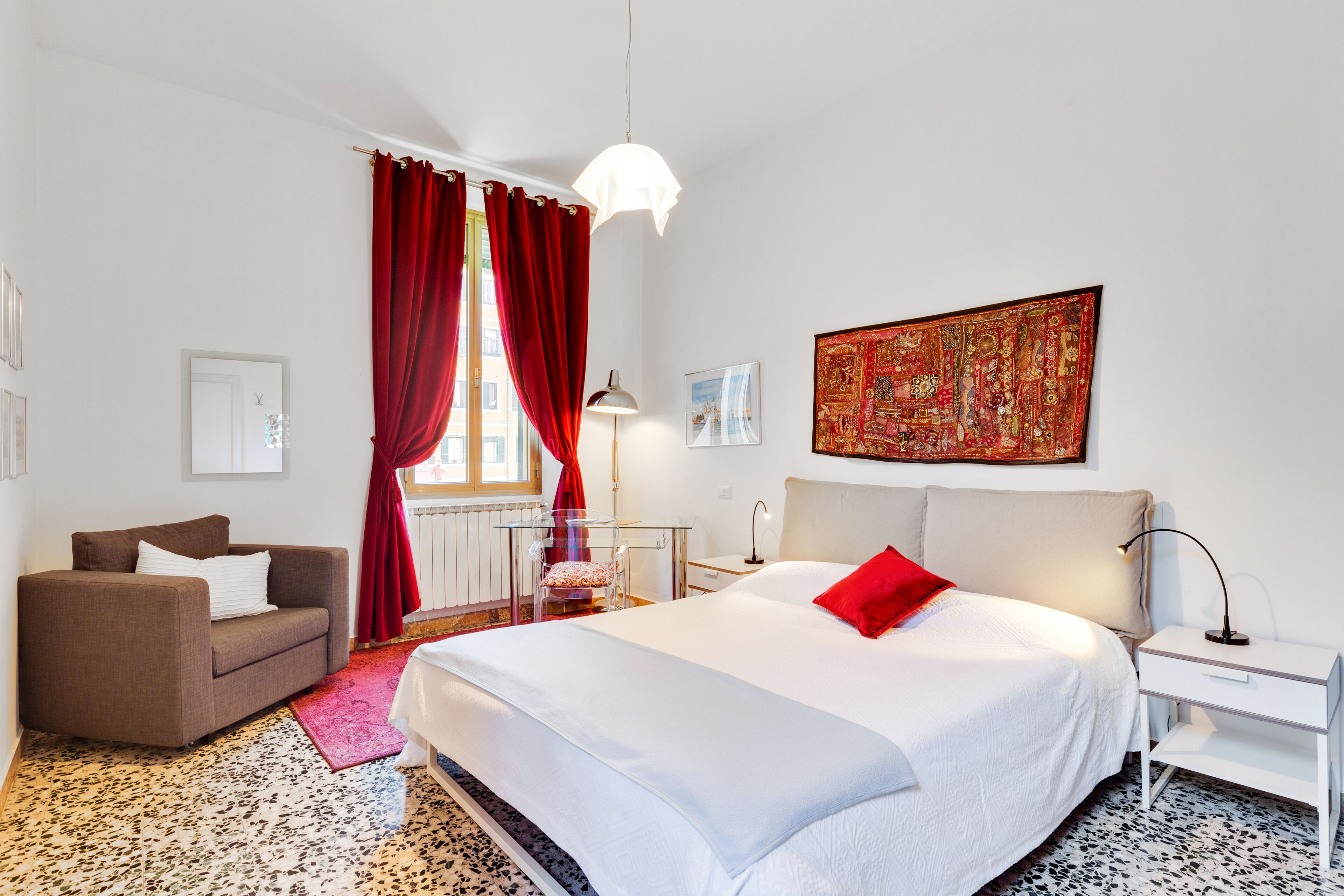 Habitación de hotel con una cama grande, un sofá, una mesita y una ventana con cortinas rojas.