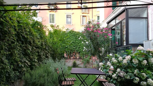 Een terras met een tafel en stoelen, omgeven door groen en bloeiende planten.