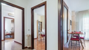 Una camera d'albergo con pavimento in legno, un termosifone, un'area pranzo con tavolo e sedie e vista sul soggiorno attraverso una porta aperta.
