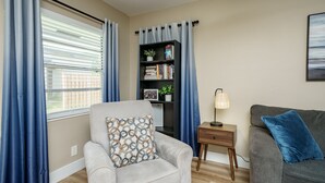 Een woonkamer met een grijze fauteuil, een grijze bank, een boekenkast en een lamp.