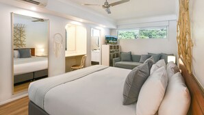 A bedroom with a large bed, a ceiling fan, a wardrobe, a desk, and a window with a view of greenery.