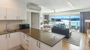 A modern kitchen with a central island, a dining area with a view, and a balcony with a scenic ocean view.