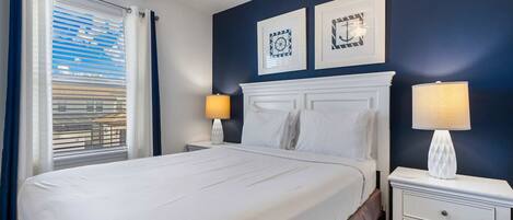 A hotel room with a bed, two bedside lamps, a nightstand, and a window with curtains.