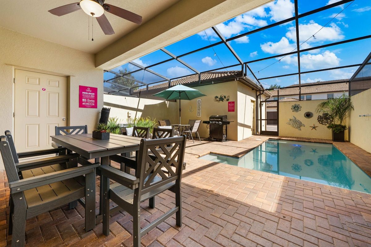 An indoor pool area with a ceiling fan, a dining table with chairs, and a small pool with decorative tiles.