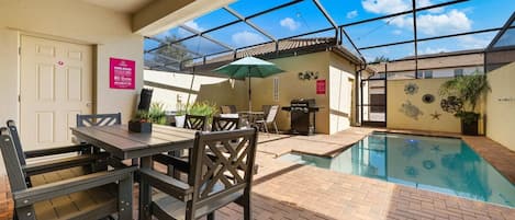 An indoor pool area with a ceiling fan, a dining table with chairs, and a small pool with decorative tiles.