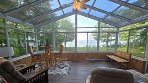 Une véranda dotée d’un ventilateur de plafond, de meubles en bois et offrant une vue sur le lac.