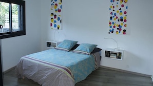 Un dormitorio con una cama, dos almohadas, una mesita de noche, una lámpara y dos cuadros en la pared.