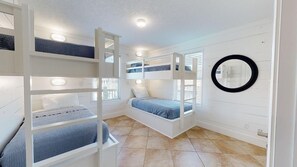 A room with bunk beds, a round mirror, and a window with blinds.