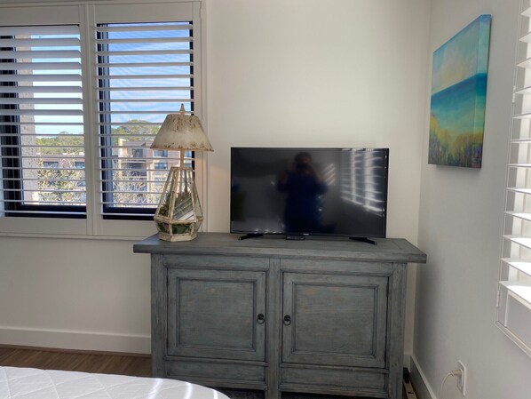 Una habitación con televisión sobre un mueble, una lámpara y un cuadro en la pared.