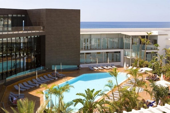 A modern hotel with a pool area, lounge chairs, and a view of the sea.