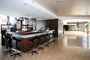 A modern bar area with a long counter, multiple bar stools, and a well-stocked bar.