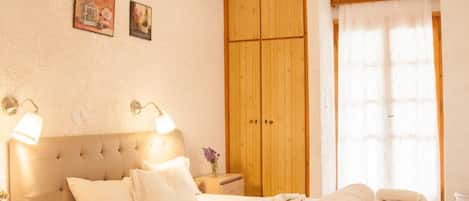 A bedroom with a bed, wooden wardrobe, bedside lamps, and a window with curtains.