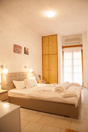 A bedroom with a bed, wooden wardrobe, bedside lamps, and a window with curtains. - Gioma Hotel (Agios Vasileios)