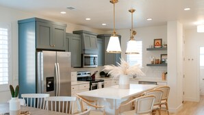Une cuisine moderne avec des meubles gris, des appareils en acier inoxydable, un îlot central doté de chaises et des luminaires suspendus.
