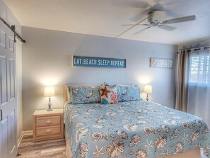 A bedroom with a bed, two bedside tables, a ceiling fan, and wall decorations.