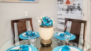 Een eettafel met blauwe placemats, een vaas met blauwe bloemen en een decoratie van een kreeft aan de muur.