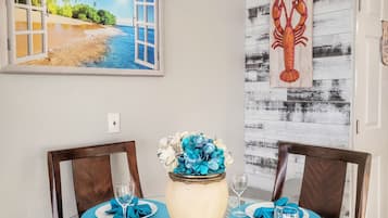 Une table à manger avec des sets de table bleus, un vase rempli de fleurs bleues et une décoration représentant un homard accrochée au mur.
