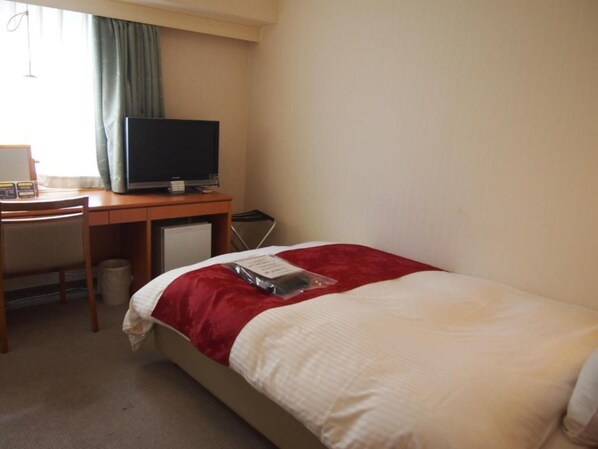 Ein Hotelzimmer mit einem Bett, einem Schreibtisch mit Fernseher, einem Sessel und einem kleinen Tisch.