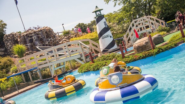 A water park with inflatable rafts, a lighthouse, and a wooden bridge.