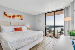 Relax in this serene hotel room featuring a large bed, framed artwork, and a sliding glass door leading to a balcony with a sea view.