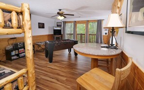A cozy room with a foosball table, a small bar area with a round table, and a bookshelf with various items.
