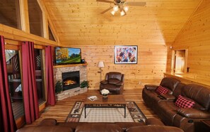 A cozy cabin interior with a stone fireplace, leather furniture, and wooden walls.