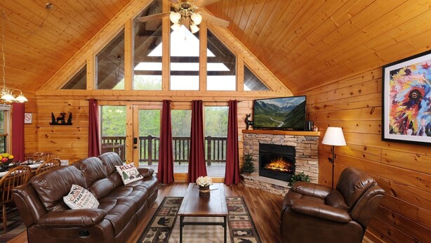 Een gezellig interieur van een chalet met een stenen openhaard, leren banken, een televisie en een eethoek.