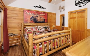 A log cabin-style room with a bed, wooden walls, a moose painting, and a sign reading "Siesta Ridge".