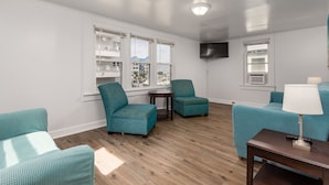 A modern living room with teal upholstered chairs, a wooden coffee table, and a flat-screen TV mounted on the wall.