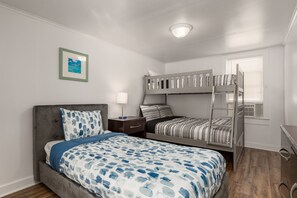 Un dormitorio con una cama individual, una cama litera, una mesita de noche, una lámpara y un cuadro en la pared.