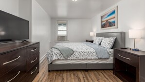 A modern bedroom with a large bed, a TV, a bedside table, and a window with blinds.