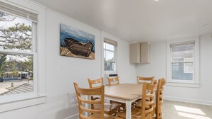 A dining area with a wooden table and chairs, a painting on the wall, and windows with blinds.