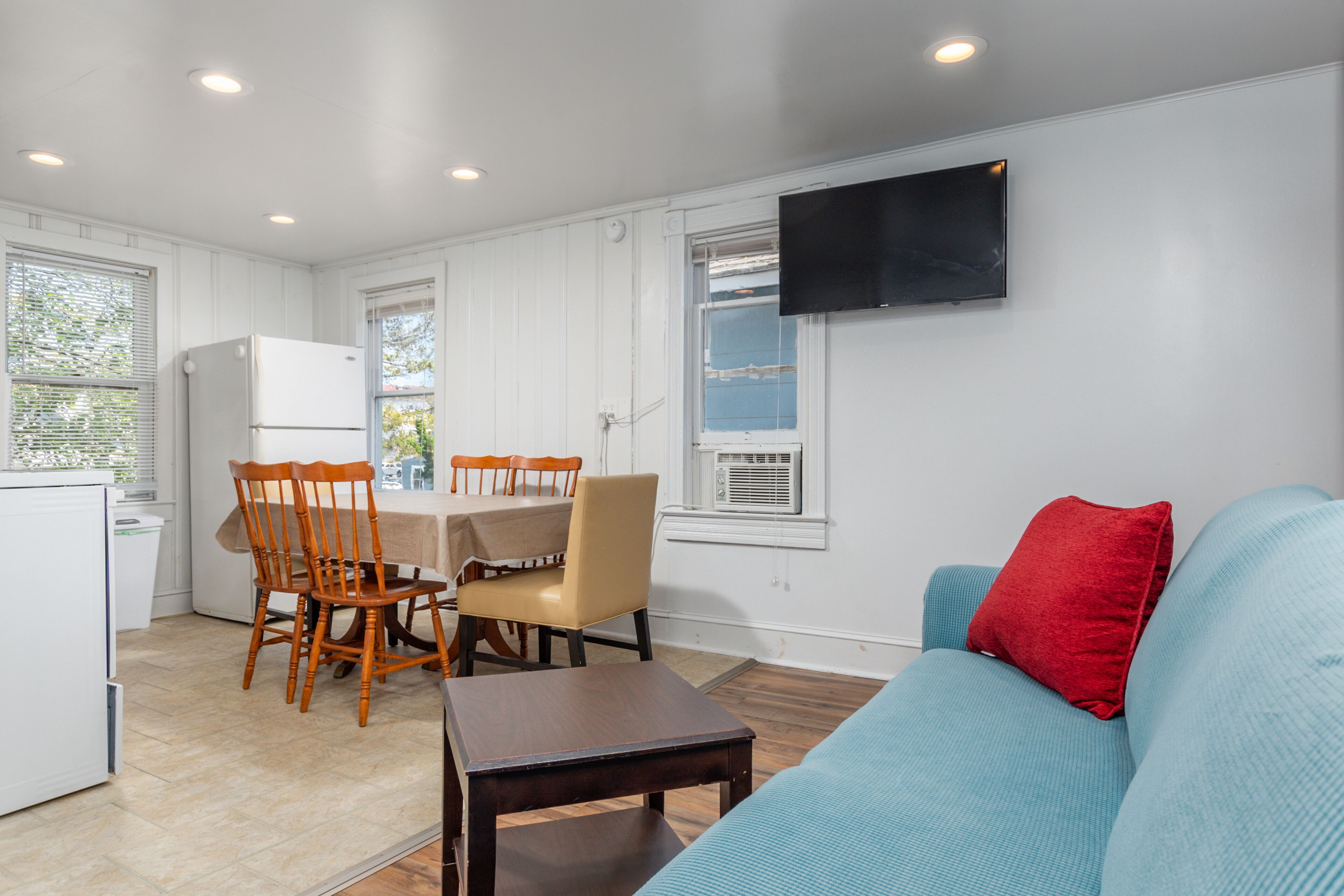 A compact living space with a kitchenette, dining area, and a sofa with a red pillow.