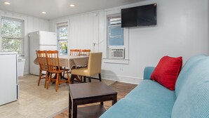 Un espacio habitable compacto con kitchenette, comedor y un sofá con un cojín rojo.
