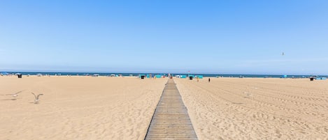 A beach with a wooden walkway leading to the sea, sandy beach, and clear blue sky.