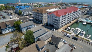 Un pueblo costero con un hotel de varios pisos destacado, que cuenta con un techo rojo, situado cerca de un puerto deportivo con barcos amarrados.