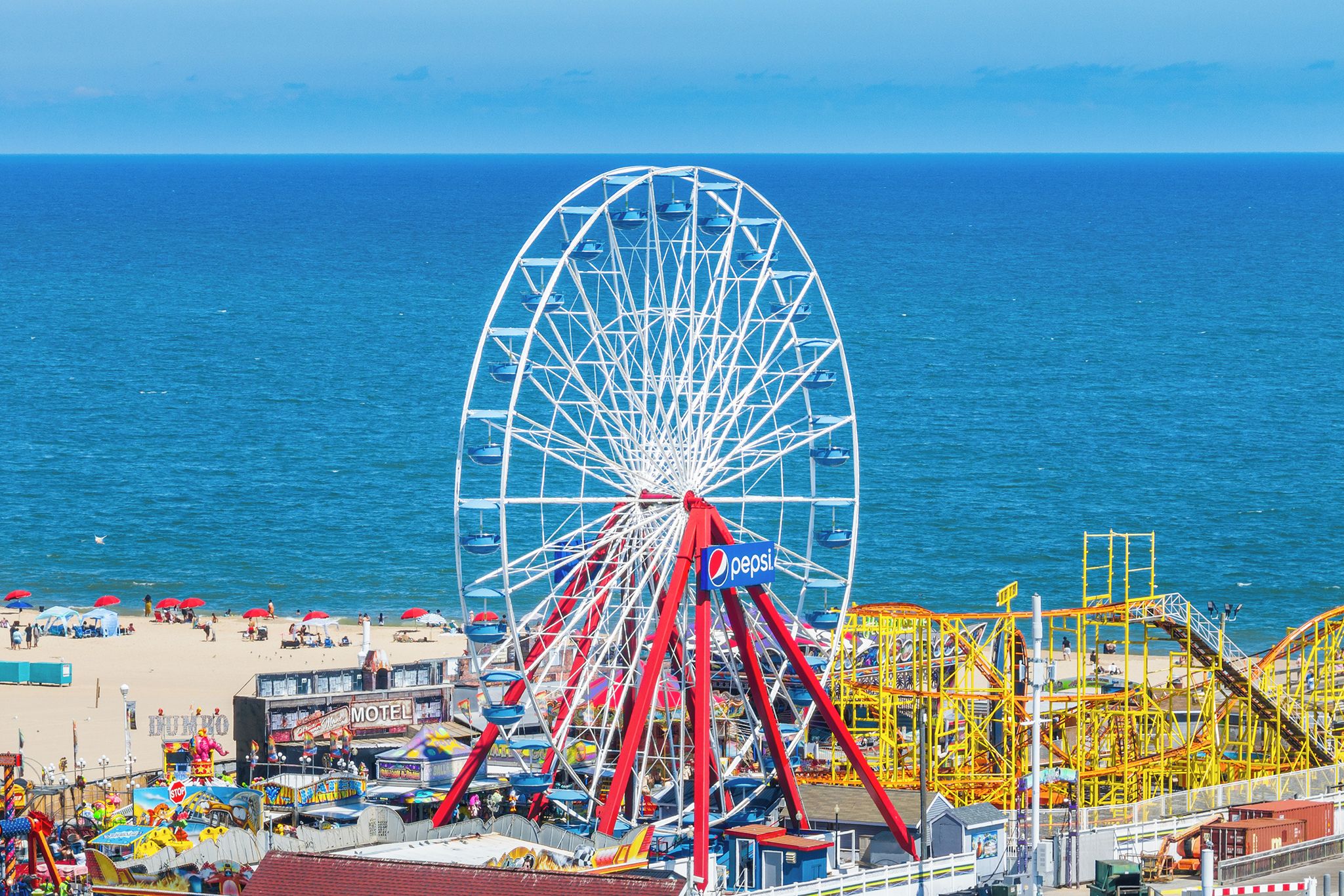 A beach with a large Ferris wheel, a roller coaster, and various beachside activities.